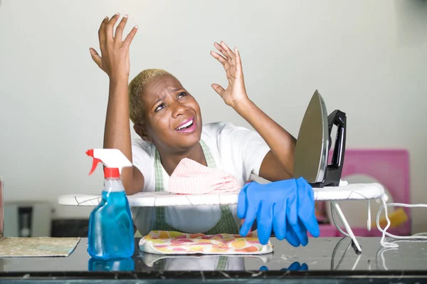 young beautiful sad and desperate black African American woman stressed working frustrated at kitchen with iron board in domestic stress feeling tired and overworked housewife concept