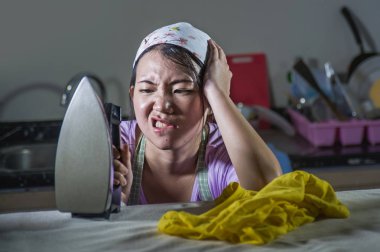 evde Mutfak Ütü giyim umutsuz ve bunalmış evde hizmetçi servisi ev ve aile içi stres çalışan genç oldukça sinirli ve gergin Asyalı Koreli kadın portresi