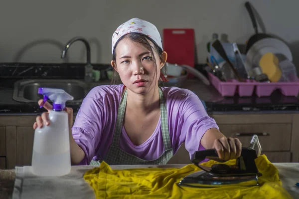 portrait of young pretty frustrated and stressed Asian Korean woman working at home kitchen ironing clothes desperate and overwhelmed in house maid service housework and domestic stress