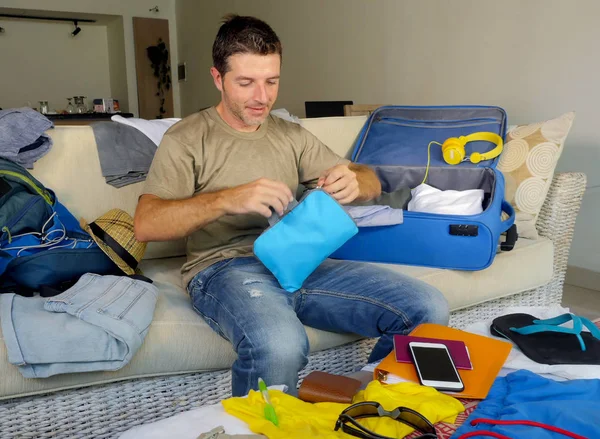 young attractive and happy man at home couch preparing travel back and packing suitcase folding clothes and organizing passport and things before leaving on holidays trip and travel concept