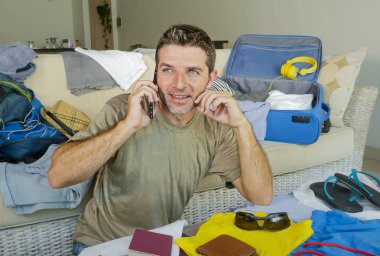 Genç yakışıklı ve mutlu bir adam seyahat bavul giyim ve yaz tatil gezi ve yolculuk tutkusu kavramı şeyler organize paketleme sırasında cep telefonu üzerinde arkadaşıyla konuşurken