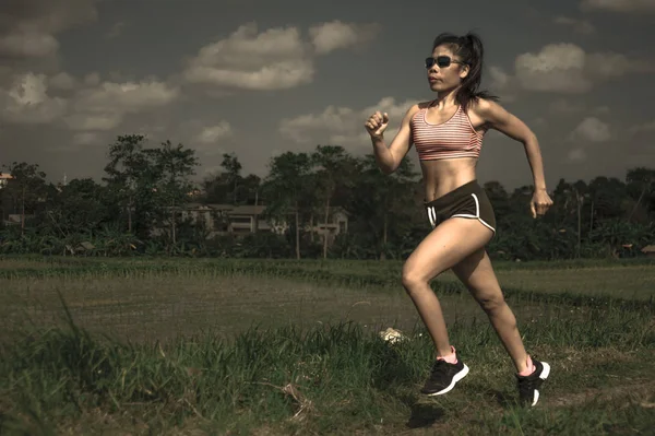 athletic and fit runner Asian woman training running series workout working hard outdoors on field background in harsh contrast light sport advertising style on energy and sacrifice concept