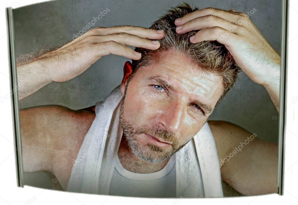 lifestyle isolated portrait of attractive worried and concerned Caucasian man looking at bathroom mirror finding gray hair frustrated in unhappy aging getting grey hairs and body care concept