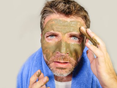 Genç dağınık komik adam kendini banyo ayna güzellik maskesi ürün duygu iğrenç ve çirkin erkek kozmetik kavram uygulayarak yüzünde yeşil krema ile dehşete bakarak