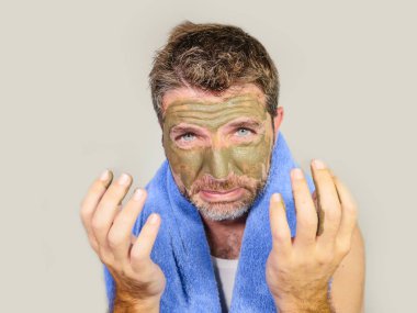 Genç dağınık komik adam kendini banyo ayna güzellik maskesi ürün duygu iğrenç ve çirkin erkek kozmetik kavram uygulayarak yüzünde yeşil krema ile dehşete bakarak