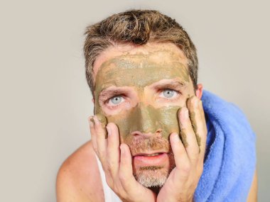 Genç dağınık komik adam kendini banyo ayna güzellik maskesi ürün duygu iğrenç ve çirkin erkek kozmetik kavram uygulayarak yüzünde yeşil krema ile dehşete bakarak