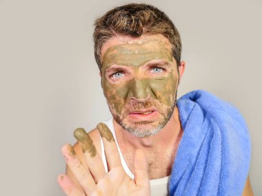 Genç dağınık komik adam kendini banyo ayna güzellik maskesi ürün duygu iğrenç ve çirkin erkek kozmetik kavram uygulayarak yüzünde yeşil krema ile dehşete bakarak