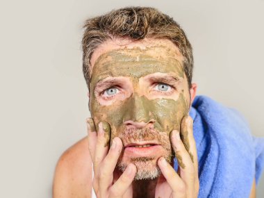 Genç dağınık komik adam kendini banyo ayna güzellik maskesi ürün duygu iğrenç ve çirkin erkek kozmetik kavram uygulayarak yüzünde yeşil krema ile dehşete bakarak