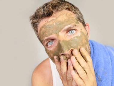 Genç dağınık komik adam kendini banyo ayna güzellik maskesi ürün duygu iğrenç ve çirkin erkek kozmetik kavram uygulayarak yüzünde yeşil krema ile dehşete bakarak