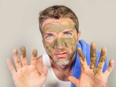 Genç dağınık komik adam kendini banyo ayna güzellik maskesi ürün duygu iğrenç ve çirkin erkek kozmetik kavram uygulayarak yüzünde yeşil krema ile dehşete bakarak