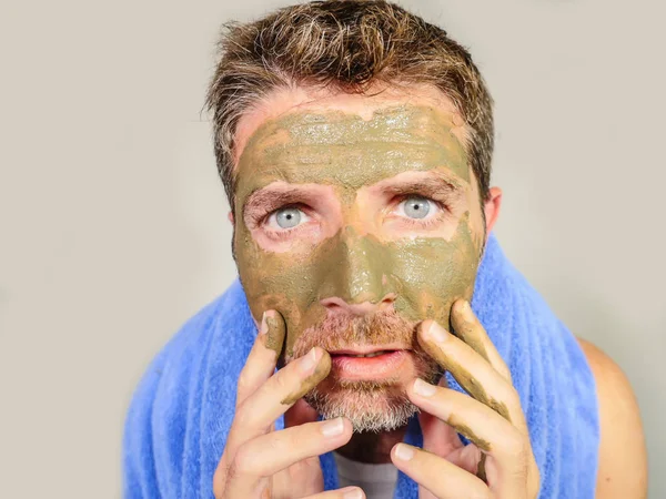 若い厄介な面白い男が見て彼自身嫌な男性化粧品コンセプトの醜い感じ美容マスク製品を適用する彼の顔に緑のクリームとバスルームの鏡でゾッとしました — ストック写真