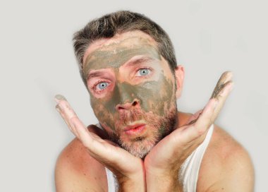 Genç komik adam kendi üzerine metroseksüel erkek alay ayna önünde poz onun yüzünde yeşil yosun maskesi ile kozmetik ve cilt bakım güzellik ürünü kullanarak 