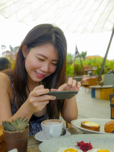 Genç güzel ve mutlu Asya Kore seyahat blogger kadının fotoğrafını cep telefonu, açık havada kahve dükkanı gülümseyen güzel kahvaltı tablo ile sosyal medya gıda yazı kavram olarak memnun