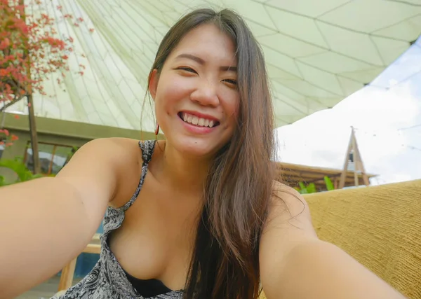 young pretty and happy Asian Korean tourist woman smiling holding mobile phone or camera taking self portrait selfie picture outdoors posing fresh enjoying beautiful holidays travel