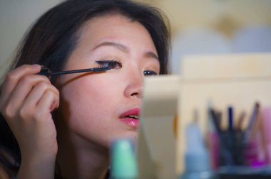 Genç güzel yaşam tarzı doğal portresi ve mutlu Asyalı Koreli kadın evde kalma dışarı gitmek için hazırlanıyor aynaya bakarak kirpik maskara makyaj uygulama