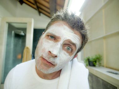 Genç komik çekici adam ev banyo tuvalet aynası sağlamlılık yüzündeki kendini tuhaf ve çirkin beyaz maske ile erkek güzellik cilt bakım ve hijyen kavramında bulma uygulama bakarak