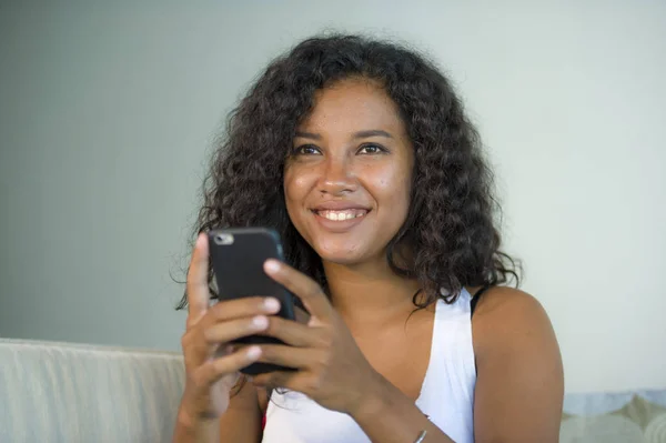 lifestyle isolated portrait of young happy and beautiful latin woman at home using mobile phone networking and texting relaxed on couch smiling cheerful enjoying internet social media app