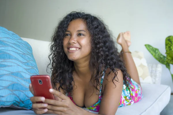 lifestyle portrait of young happy and beautiful black african american woman networking at home using internet mobile phone texting relaxed on sofa couch smiling cheerful enjoying social media