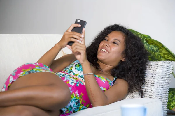 lifestyle portrait of young happy and beautiful latin woman networking at home using internet mobile phone texting relaxed on sofa couch smiling cheerful enjoying social media app