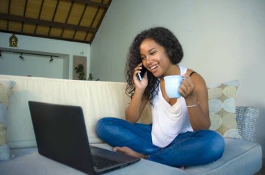 cep telefonu evde dizüstü bilgisayarda çalışırken oturma odası koltuk kanepe genç mutlu ve güzel siyah afro Amerikan kadın söz yaşam tarzı izole portresi 