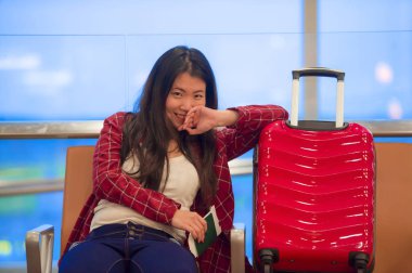 Genç güzel ve mutlu Asyalı Koreli turist kadın ile gidiş neşeli holding pasaport gülümseyen uçuş için bekleyen oturma havaalanında bavul seyahat ve biniş kartı gezi tatil