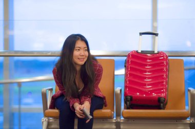 Genç güzel ve mutlu Asyalı Koreli turist kadın ile gidiş neşeli holding pasaport gülümseyen uçuş için bekleyen oturma havaalanında bavul seyahat ve biniş kartı gezi tatil