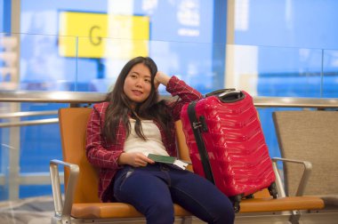 Genç güzel ve mutlu Asyalı Koreli turist kadın ile gidiş neşeli holding pasaport gülümseyen uçuş için bekleyen oturma havaalanında bavul seyahat ve biniş kartı gezi tatil