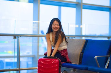 Genç güzel yaşam tarzı taze portresi ve seyahat bavul Havaalanı gidiş oturan kadınla mutlu Asyalı Koreli turist uçuş tatil gezisi neşeli gülümseyen için bekleyen gate lounge