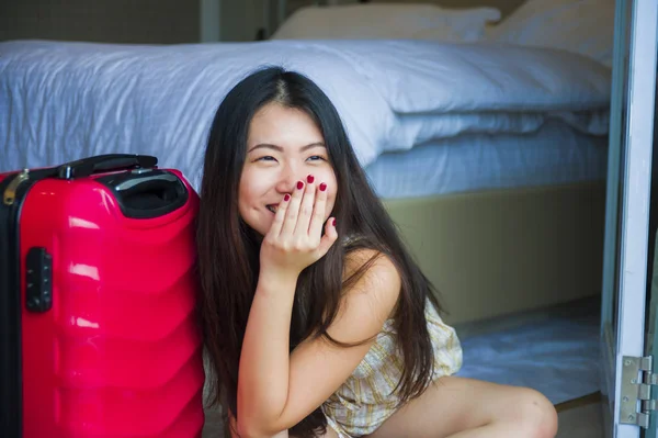 lifestyle natural portrait of young happy and beautiful Asian Korean tourist woman with travel suitcase arriving tired sitting at five star hotel floor staring the room balcony excited enjoying holidays