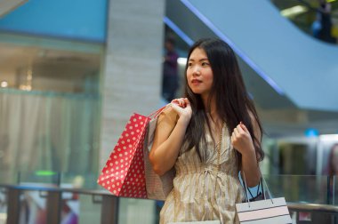 yaşam tarzı kapalı dikey genç mutlu ve güzel Asyalı Koreli kadın alışveriş merkezi moda yürüyüş neşeli satın alışveriş çantaları taşırken Alışverişkoliğin kadın kavramı içinde gülümseyen depolamak