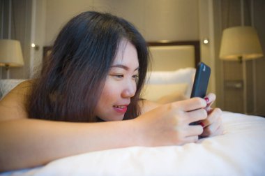 neşeli gülümseyen yatakta yatarken yatak odası ya da otel oda rahat genç mutlu ve güzel Asyalı Koreli kadın evde yaşam tarzı portresi Internet online dating app manifatura cep telefonu kullanarak.