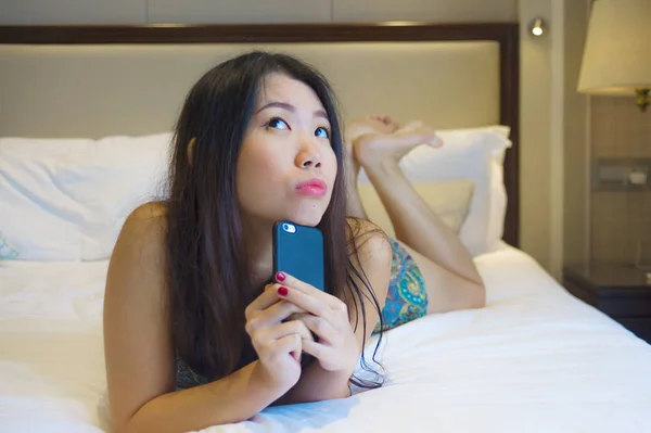 生活在家庭卧室或酒店房间的年轻快乐和漂亮的亚洲韩国妇女的生活方式肖像躺在床上轻松微笑愉快使用互联网在线约会应用程序发短信手机 — 图库照片