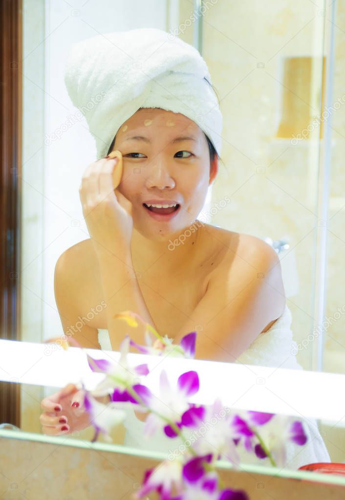 lifestyle fresh portrait of young happy and beautiful Asian Korean woman at home or hotel bathroom wrapped in toilet towel applying makeup cheerful and natural in female beauty and skin care 