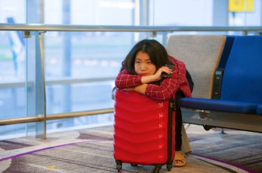 Genç mutlu portre yaşam tarzı ve bavul el bagajı tatil seyahat uçuş için bekleyen ile Havaalanı kalkış yatılı kapısında oturan güzel Asyalı Koreli turist kadın