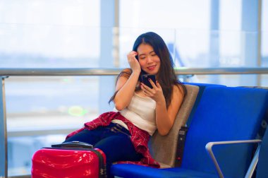 Genç mutlu ve kapısında tatil seyahat gülümseyen cep telefonunda internet kullanarak uçuş için bekleyen Havaalanı kalkış yatılı oturan pretty Asya Çinli turist kadın portre yaşam tarzı
