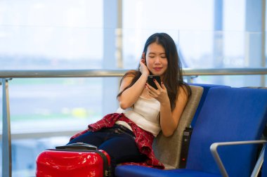 Genç mutlu ve kapısında tatil seyahat gülümseyen cep telefonunda internet kullanarak uçuş için bekleyen Havaalanı kalkış yatılı oturan güzel Asyalı Koreli turist kadın portre yaşam tarzı