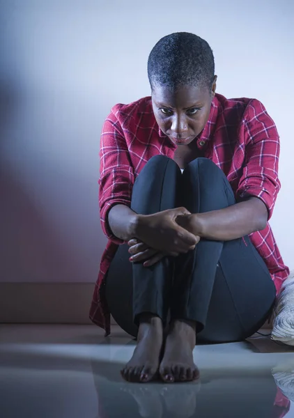 lifestyle indoors shady portrait of young sad and depressed black african American woman sitting at home floor feeling desperate and worried suffering pain and depression in dramatic light