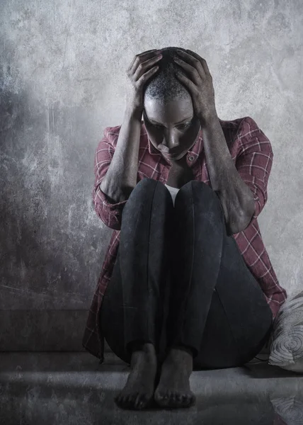 lifestyle indoors shady portrait of young sad and depressed black african American woman sitting at home floor feeling desperate and worried suffering pain and depression in dramatic light