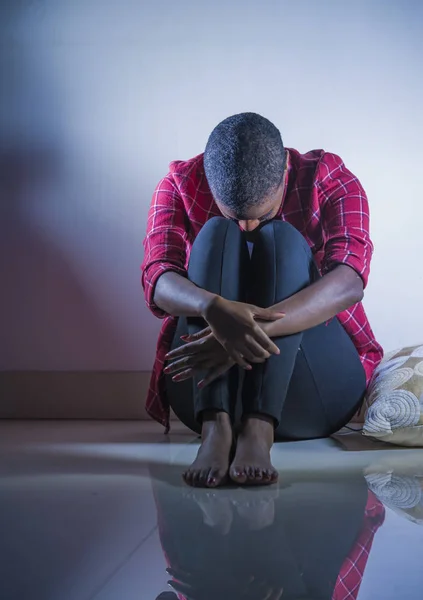 lifestyle indoors shady portrait of young sad and depressed black afro American woman sitting at home floor feeling desperate and worried suffering pain and depression in dramatic light