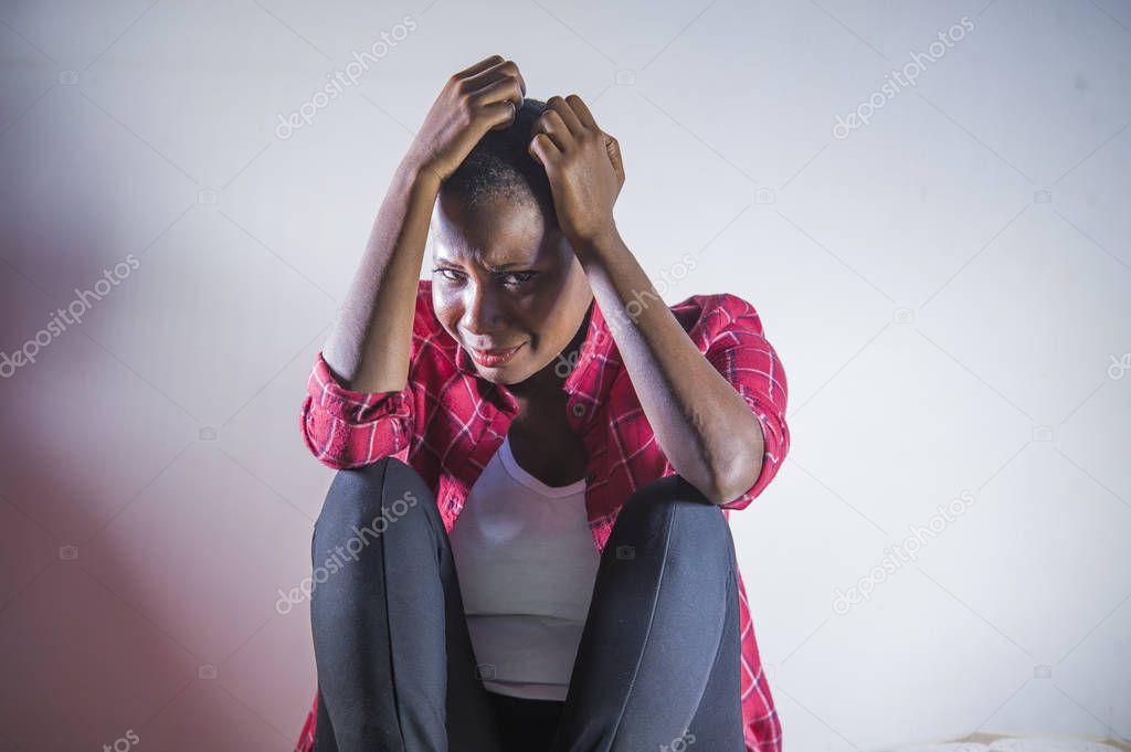 lifestyle indoors shady portrait of young sad and depressed black afro American woman sitting at home floor feeling desperate and worried suffering pain and depression in dramatic light