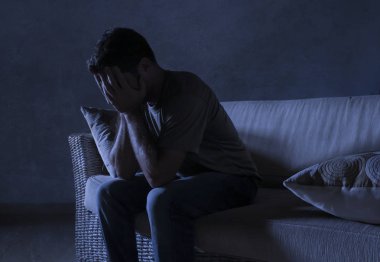 lifestyle dramatic light portrait of young sad and depressed man sitting at shady home couch in pain and depression feeling stressed and desperate crying alone suffering anxiety crisis clipart
