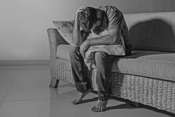 lifestyle dramatic light portrait of young sad and depressed man sitting at shady home couch in pain and depression feeling stressed and desperate crying alone suffering anxiety crisis