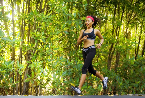lifestyle outdoors portrait of young fit and happy Asian Chinese woman with hairband training hard on asphalt road running workout at beautiful trees city park in exercise fitness and health care
