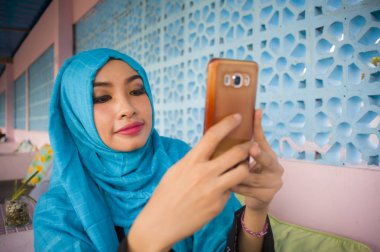 yaşam tarzı açık havada dikey genç mutlu ve güzel kadın Müslüman türban başörtüsü internet sosyal medya app kullanarak cep telefonu mesajlaşma ya da ağ metin neşeli gönderme