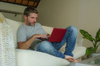 internet iş başarısı ve online serbest iş concep düşünceli gülümseyen dizüstü bilgisayar netbook ile çalışma koltuk kanepe evde oturan genç çekici ve yakışıklı mutlu adam rahat