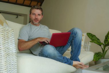 internet iş başarısı ve online serbest iş concep içinde neşeli gülümseyen dizüstü bilgisayar netbook ile çalışma koltuk kanepe evde oturan genç çekici ve yakışıklı mutlu adam rahat