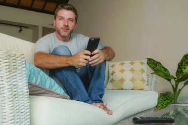 yaşam tarzı kapalı cep telefonu online app dating veya evde kanepe koltuk ile smartphone rahat oturan ağ Internet kullanan genç yakışıklı ve çekici mutlu adam portresi