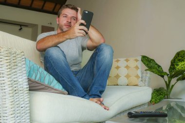 yaşam tarzı kapalı cep telefonu online app dating veya evde kanepe koltuk ile smartphone rahat oturan ağ Internet kullanan genç yakışıklı ve çekici mutlu adam portresi