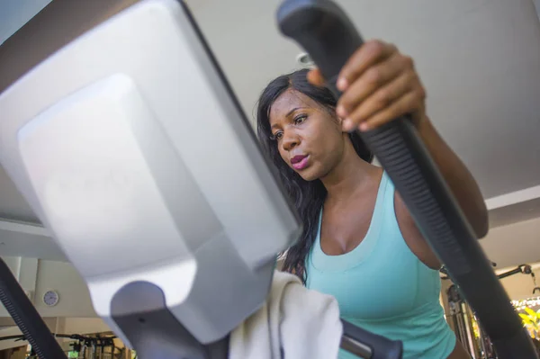 indoors gym portrait of young attractive and concentrated black african American woman training elliptical machine workout at fitness club working hard in healthy lifestyle