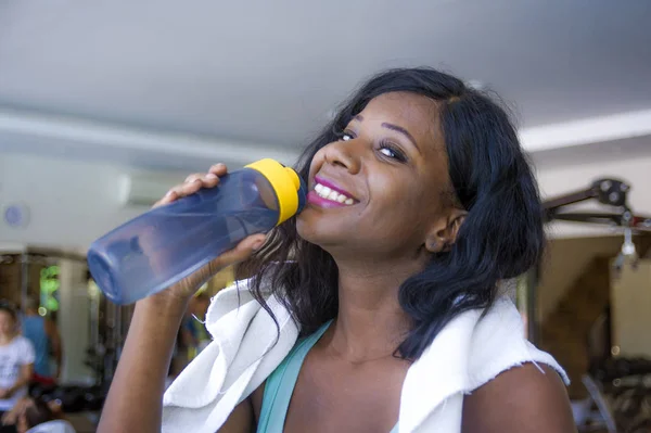屋内のライフ スタイル肖像若い幸せと魅力的な黒いアフロ アメリカ女性のハード トレーニング ボトル飲料水を押しながらフィットネス クラブで陽気な笑顔の後汗まみれのジムでトレーニング — ストック写真